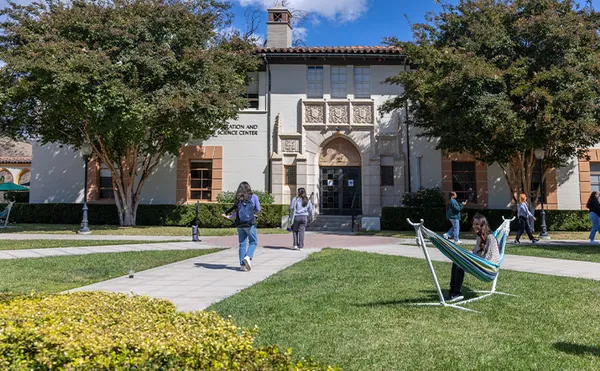 A grassy plaza in front of a large building with students milling around.
