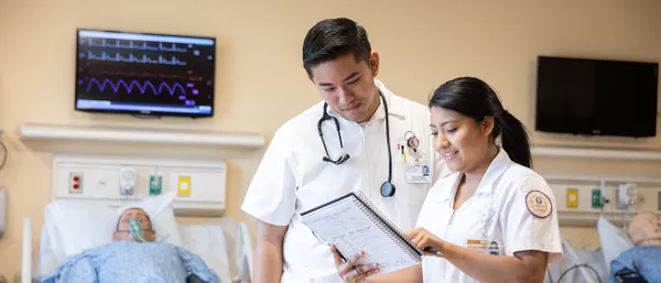 Two health professionals looking at a note pad in a hospital room.