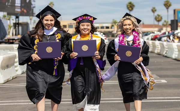 Three students walking and showing their diplomas at the 2022 Commencement