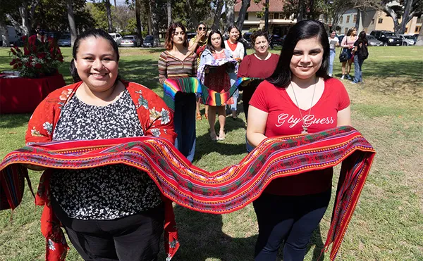 Two students holding a long red cloth and walking towards the camera.