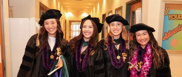 four MSMU graduates smiling in their robes