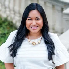 A protrait of a woman in a white top standing in front of stairs