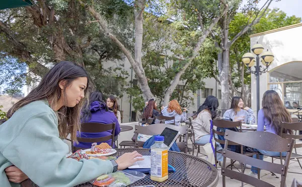 Students sitting under trees at tables eating lunch