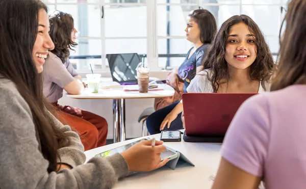 Students studying around several tables in front of large windows