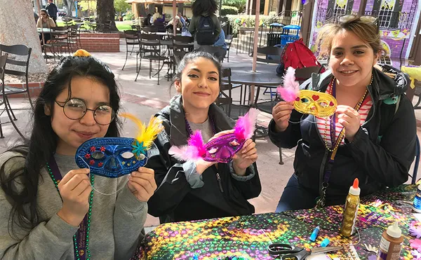 Three students holding up brightly colored masquerade masks which they made