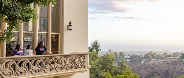 Three students standing on a balcony overlooking a landscape which streatches to the horizon