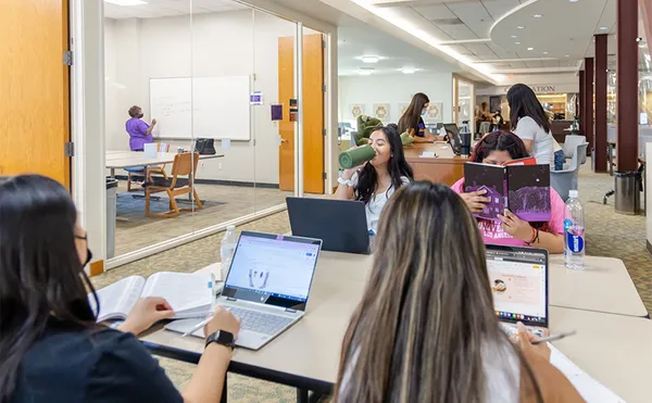 Students sitting at tables and studying in a library.