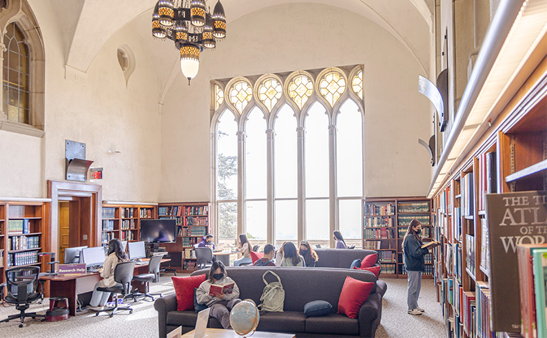 Students reading in front of a large floor to ceiling window in a library.