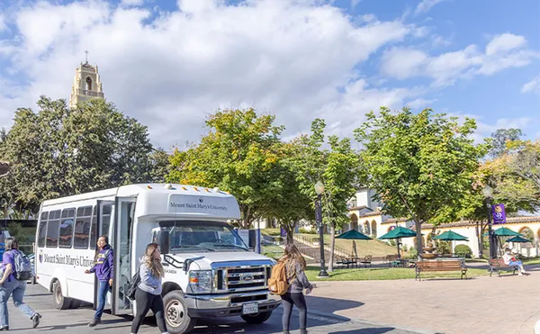 Students getting off an MSMU shuttle bus with trees and a bell tower in the background