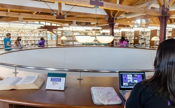 A student using their laptop in a large central area in a library