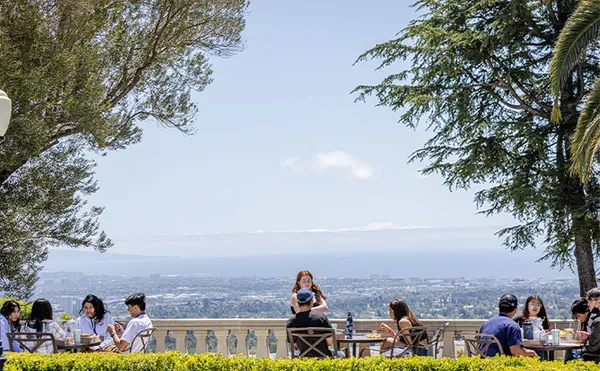 Students sitting around tables eating lunch with a large landscape in the background