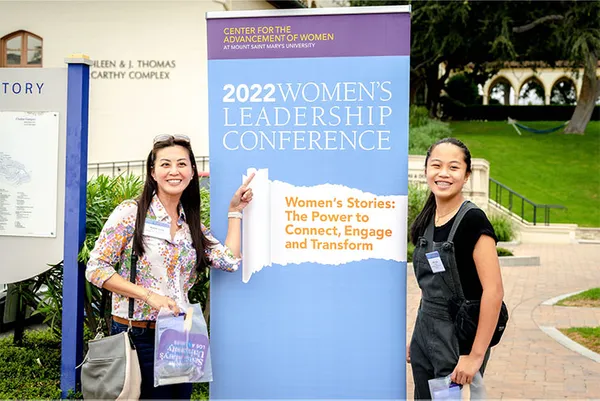 two students smiling with Women's Leadership Conference poster
