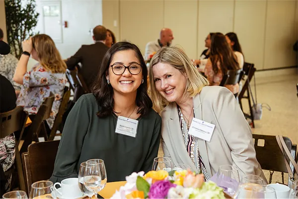 two female alumnae smiling seated at table