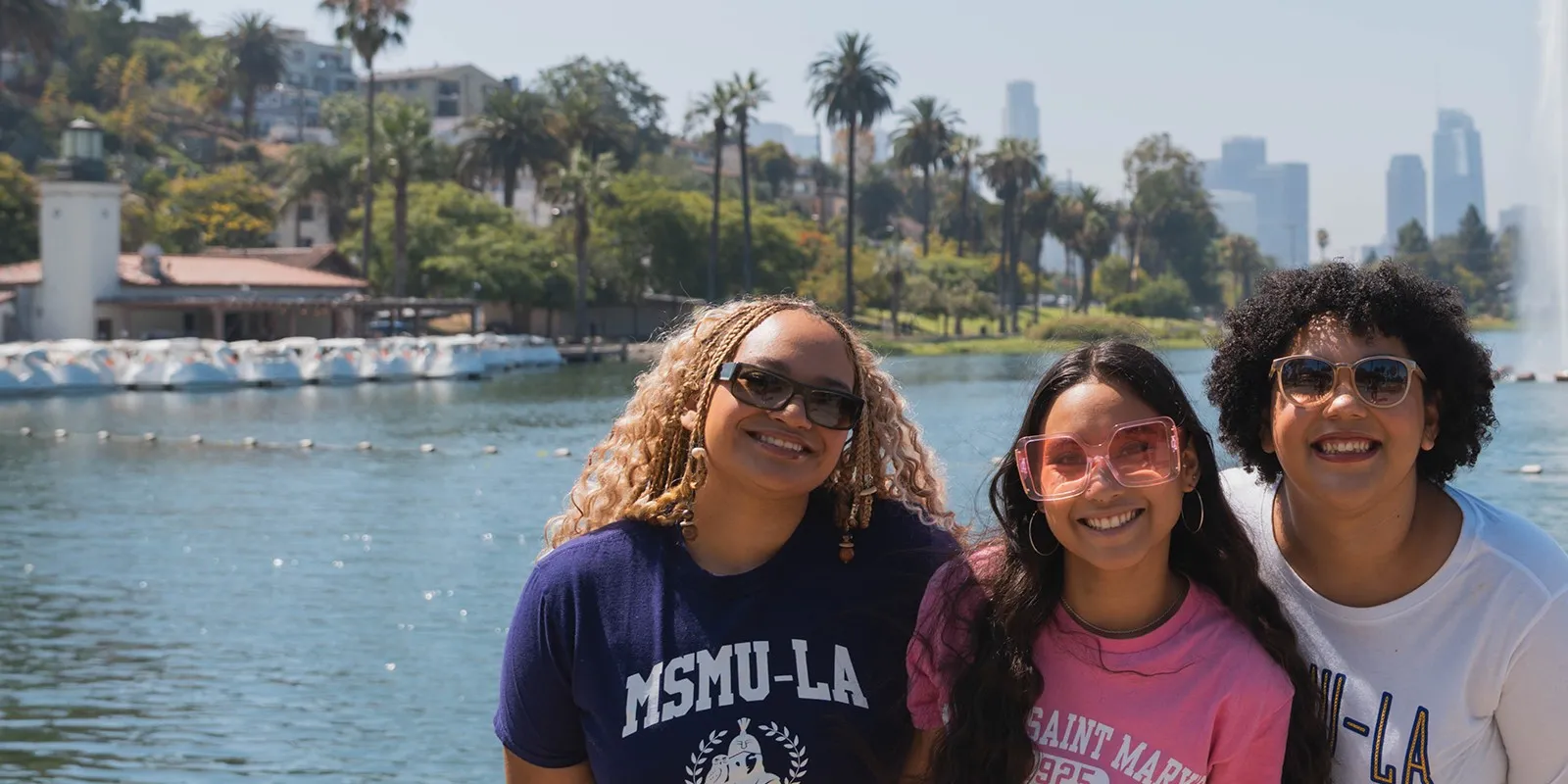 three female students smiling in front of Los Angeles lake wearing MSMU shirts