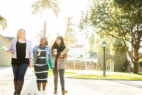 three female students walking and smiling on campus