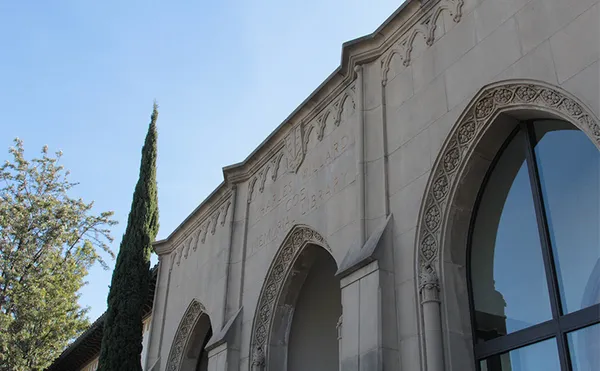 The front of a stone building with arched windows and text over the entryway which reads 