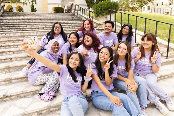 students sitting on the ground in purple MSMU shirts smiling for a photo