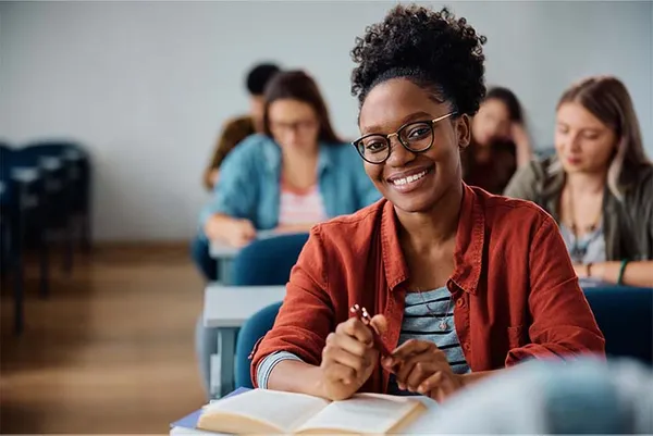 woman smiling in a classroom with fellow students behind her.