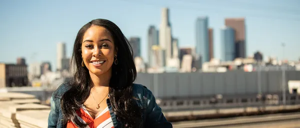 A woman standing outside smiling with the Los Angeles skyline in the background.