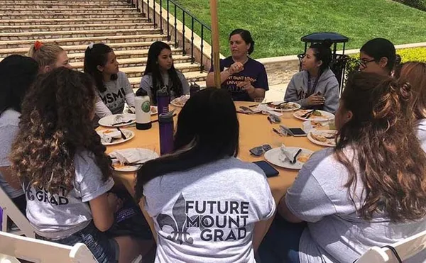 group of students sitting at table outside listening to a speaker