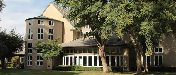 A rounded building with large windows seen through tall trees.
