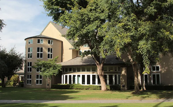 A rounded building with large windows seen through tall trees.