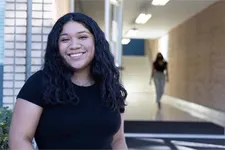 female student smiling standing in front of entrance to academic building
