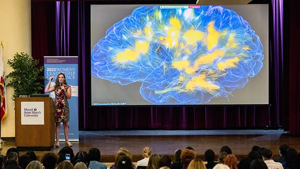 speaker giving presentation on stage with powerpoint showing the human brain
