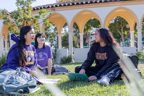 female students chatting and sitting on grass on campus